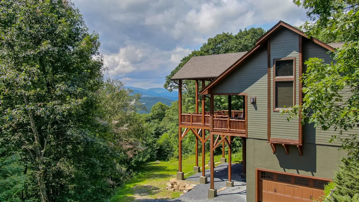 An inviting elevated porch overlooks surrounding greenery and distant mountains, creating a serene setting for relaxation or gathering. The view underscores a direct connection to the beautiful mountain landscape.