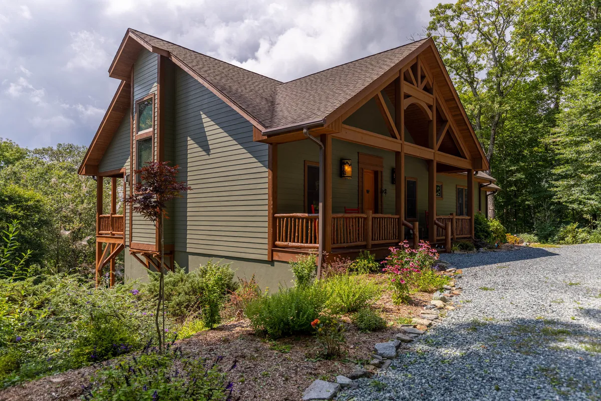 The hero image showcases the inviting front porch of a beautiful single-family mountain home, surrounded by lush landscaping and nestled in the tranquil North Carolina woods. The scene features comfortable seating, a welcoming entrance, and hints of the expansive, walkable property, setting the stage for relaxation and outdoor enjoyment.