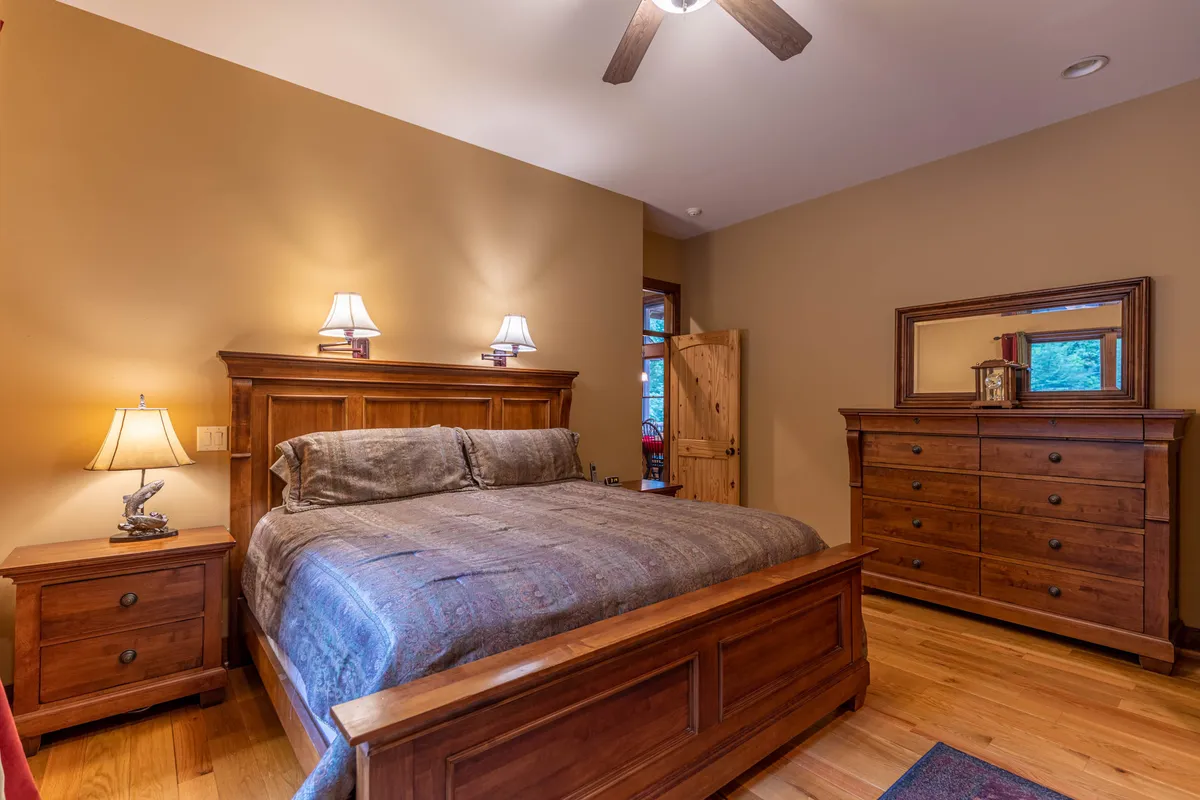 A simple, inviting bedroom with a neatly made bed, a nightstand and lamp for bedtime reading, a dresser, and a door leading to other parts of the suite. The space promises comfort, with a focus on restful sleep and relaxation.