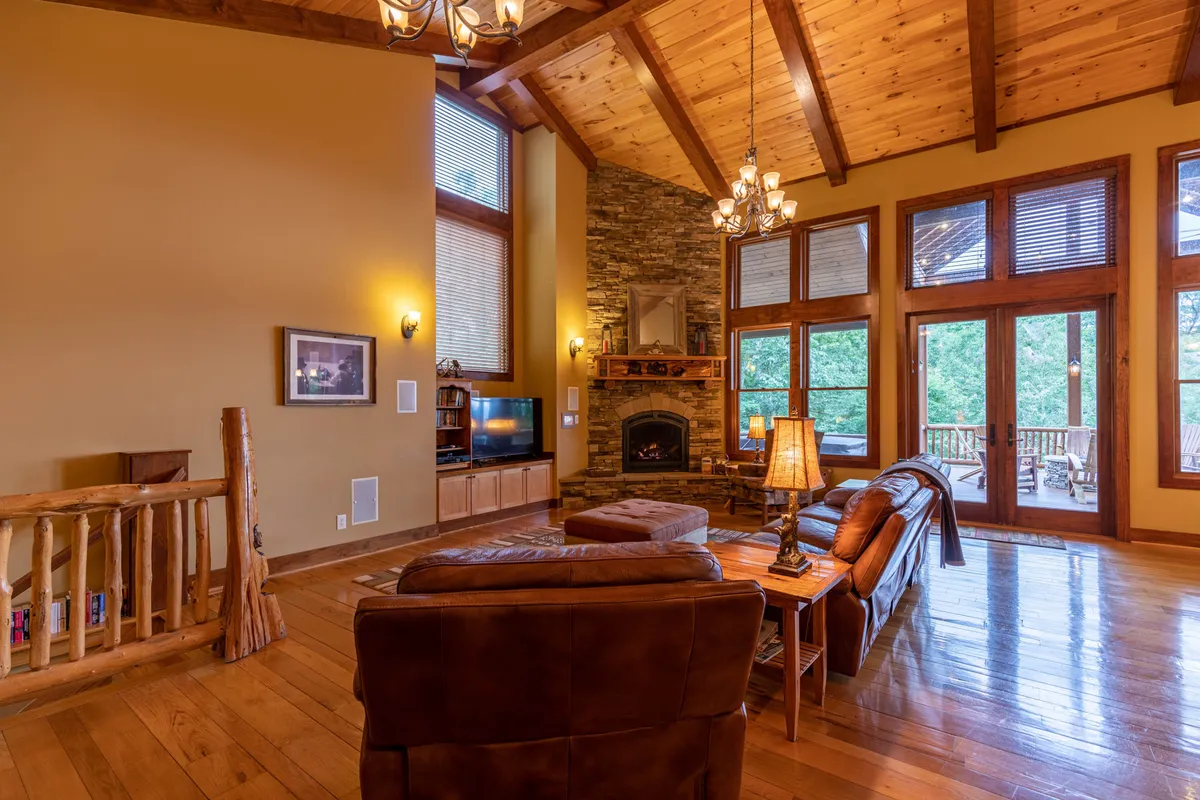 This interior image showcases a spacious living area with a striking stone fireplace, large windows that likely frame views of the outdoors, exposed wooden beams, and a comfortable seating arrangement. The atmosphere is warm and inviting, suggesting a cozy place to unwind after a day spent outdoors.