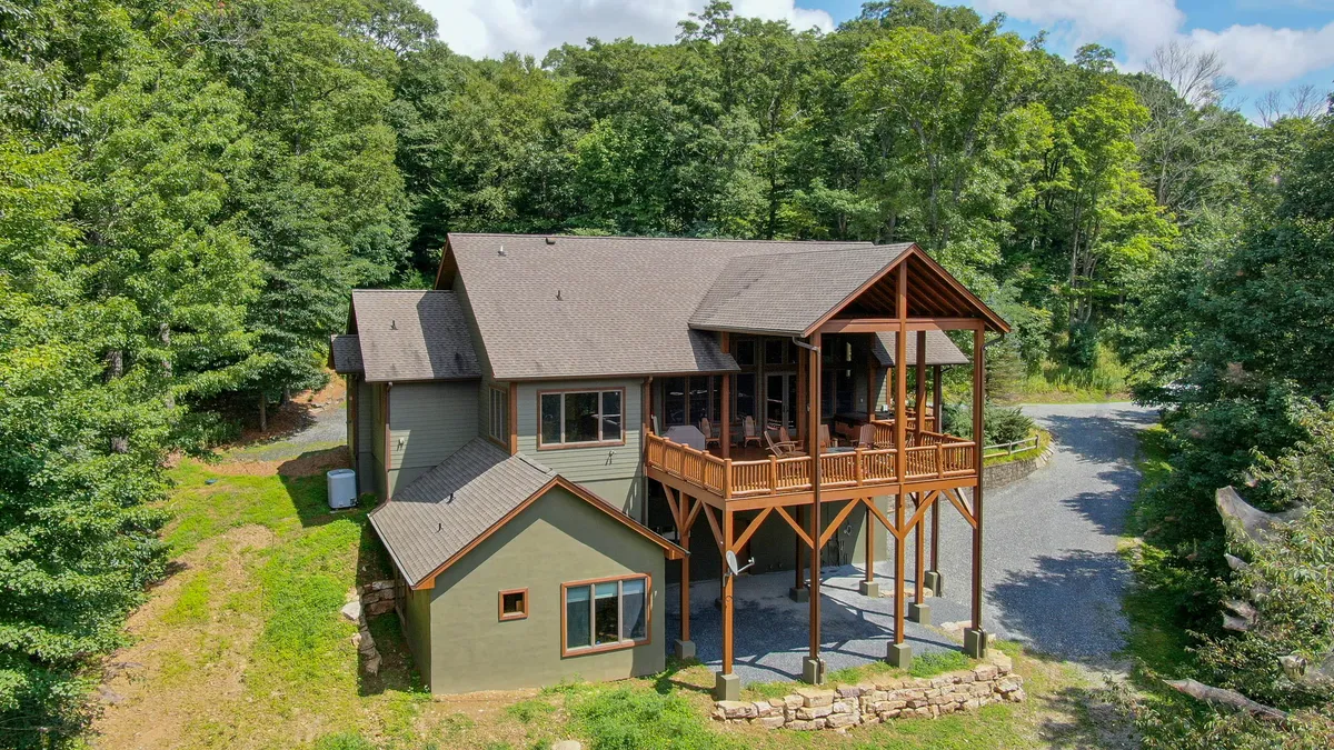 A spacious wooden deck is surrounded by trees, with a stone pathway leading up to it. The area is set for relaxation or gatherings, ideal for enjoying fresh air, sunset views, or evening socializing.