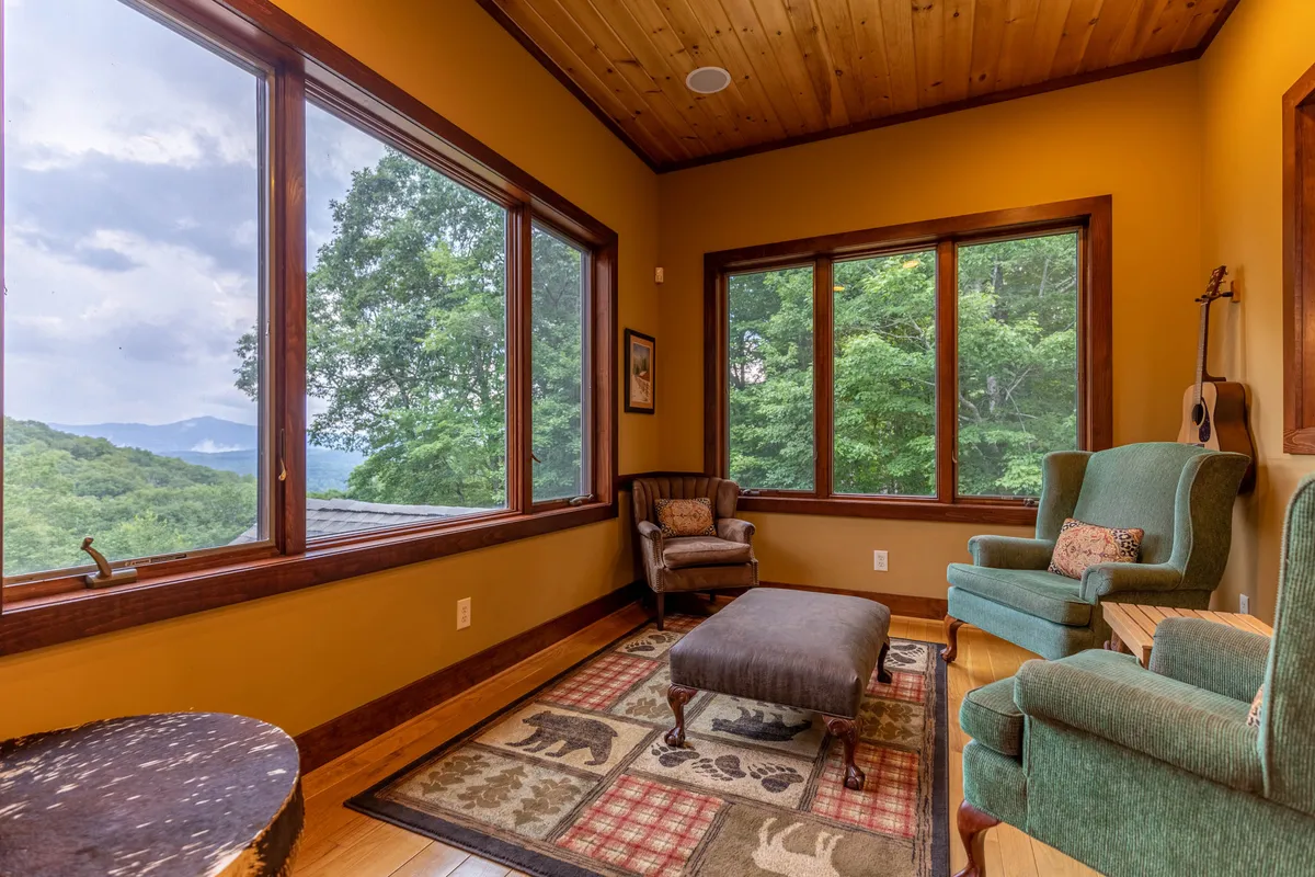 A serene lounge area with comfortable seating arranged beside large picture windows that frame breathtaking mountain views. The space is designed for relaxation, conversation, and soaking in the tranquil landscape, with a textured area rug adding warmth to the ambiance.
