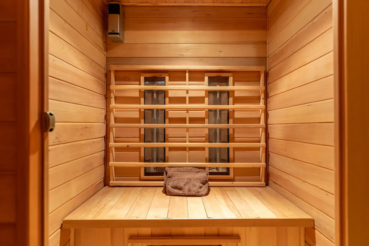 A close-up view of a classic wood-paneled sauna, complete with a wooden bench and heating element, evoking tranquility and warmth. Towels are neatly placed, reinforcing the focus on comfort and self-care.