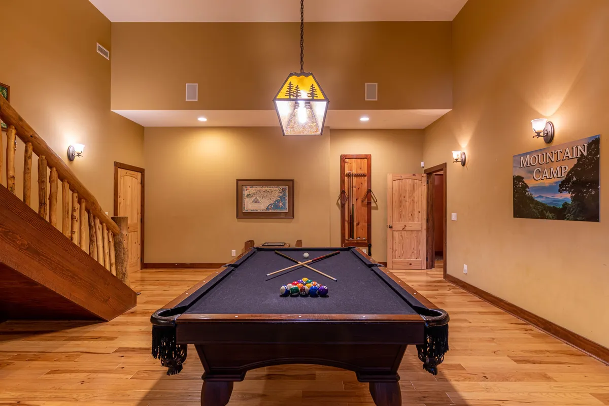 A friendly, casual game room scene centered around a pool table, illuminated by a chandelier and accentuated with playful signage. The comfortable setting invites guests to gather, play, and celebrate together.