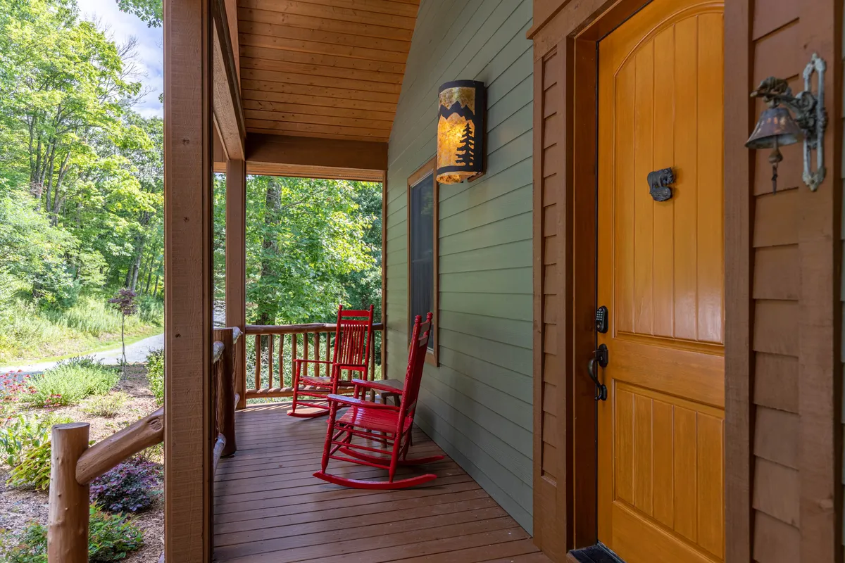 A welcoming front porch with red rocking chairs and a decorative light fixture sits beside the main entrance. The porch overlooks lush greenery, creating a tranquil space ideal for greeting guests or unwinding after a celebration.