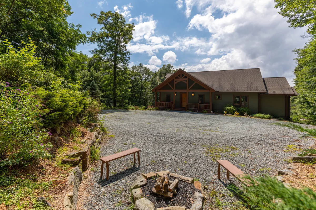 The house facade framed by trees, featuring a cozy fire pit with surrounding benches. The mood is inviting, and the scene suggests outdoor relaxation, gathering with loved ones, or enjoying tranquil mornings and evenings.